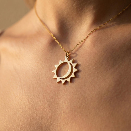 May include: A gold-colored necklace featuring a sun and crescent moon pendant. The pendant has a sunburst design with a crescent moon cutout. The necklace is worn around the neck and is a delicate piece of jewelry.