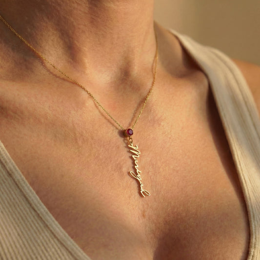 Vertical name necklace with round red garnet birthstone, gold custom script nameplate pendant on model, personalized mothers day gift for women