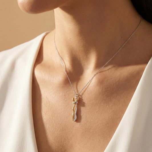 May include: A silver necklace with a pendant featuring a gold and silver intertwined figure. The pendant hangs from a delicate silver chain. The necklace is displayed against a white background.