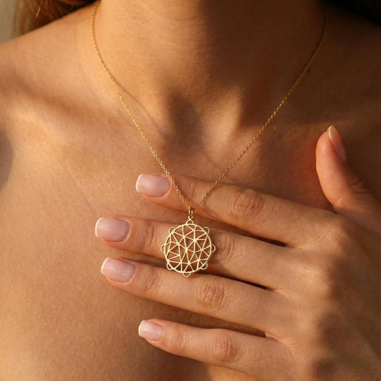 May include: A gold-colored necklace with a geometric pendant. The pendant features an intricate openwork design of interconnected lines and shapes. The necklace is worn around the neck and rests on the chest.