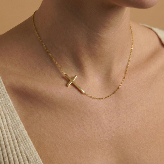 Close up of gold sideways cross pendant, delicate chain jewelry for layering, modern faith necklace flat lay