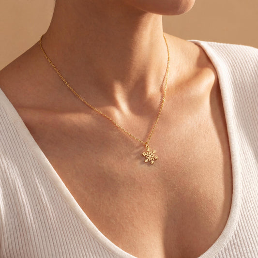 Dainty 14K gold plated snowflake pendant necklace resting elegantly on a woman's collarbone, showing a minimalist geometric jewelry design perfect for a unique Mother's Day gift or layered everyday wear.