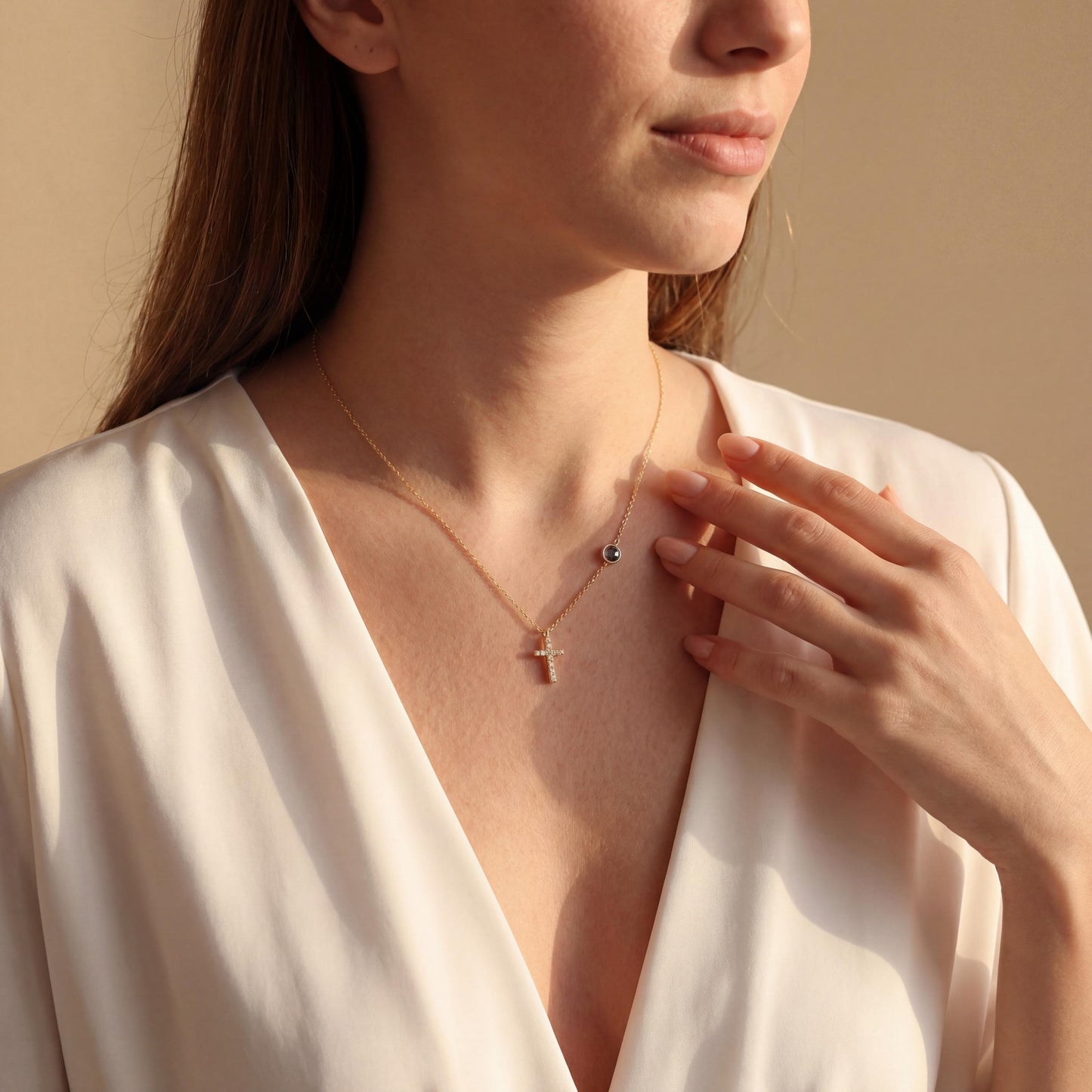 Dainty gold chain necklace featuring a small pave diamond cross pendant and a round bezel-set birthstone charm, worn by a model. Personalized minimalist religious jewelry.