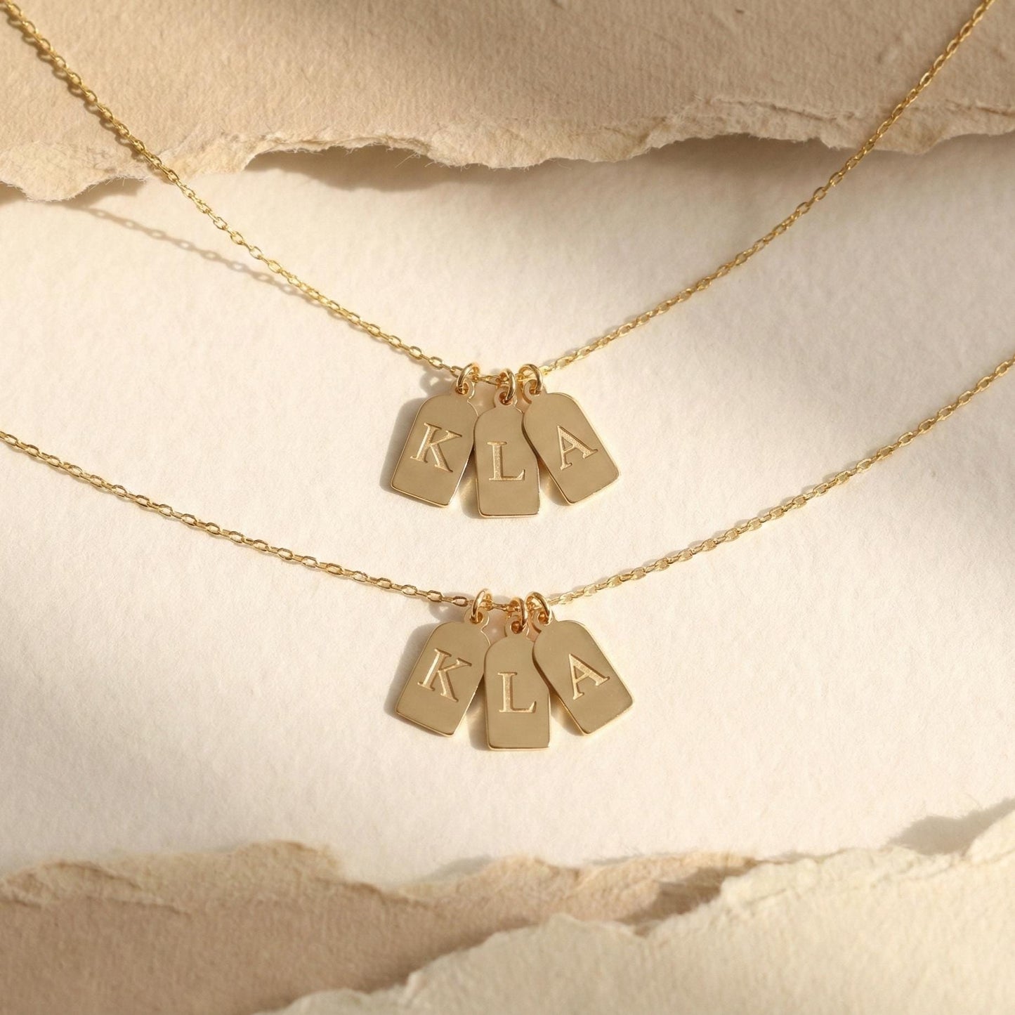 Gold initial necklace featuring three small rectangular pendant tags engraved with letters K L A, worn on a woman's neck, minimalist personalized jewelry for mom