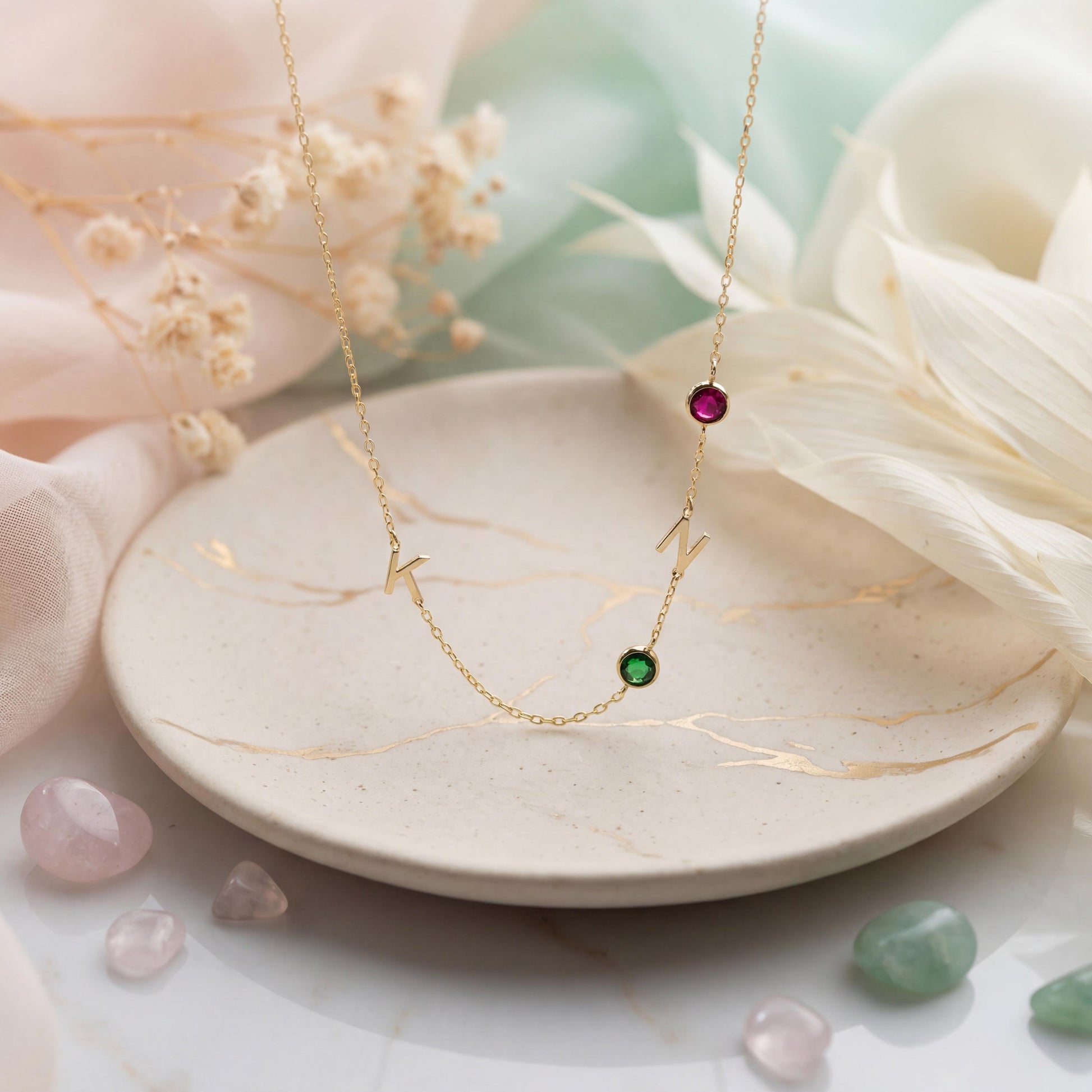 Dainty gold necklace featuring sideways initials and bezel set birthstones, personalized family jewelry for mother's day gift, minimalist custom letter necklace with ruby and emerald colored stones on neck.