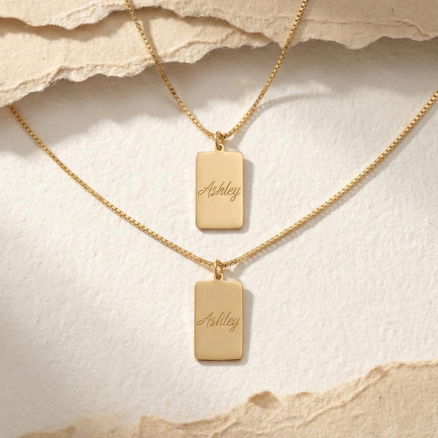 Gold vertical bar necklace on a model's neck, personalized with the engraved name Ashley in cursive font. Minimalist rectangular pendant gift for mother's day.