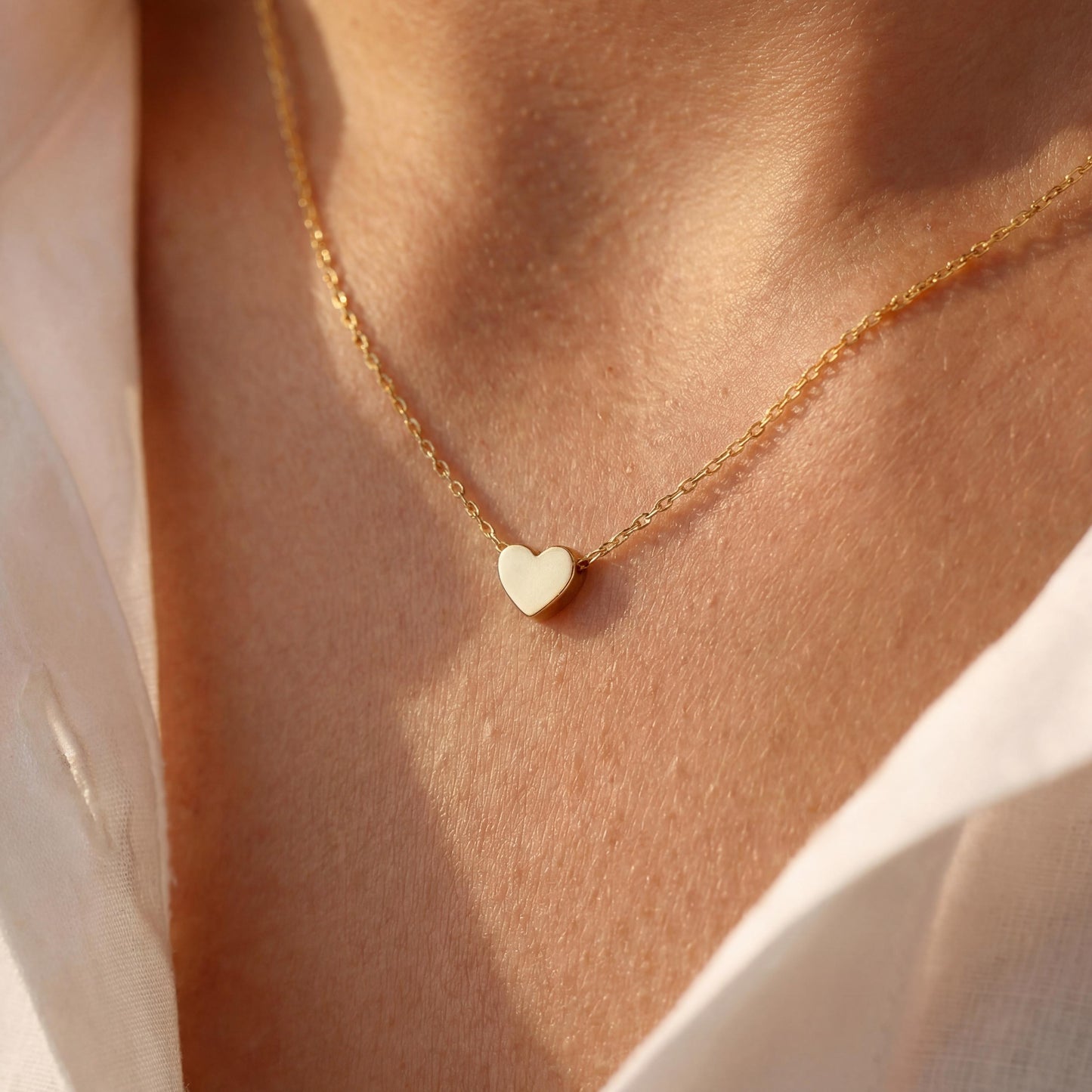 Minimalist 14k gold plated tiny puff heart necklace on a model wearing a white shirt, dainty gold choker chain detail, small heart pendant close up, perfect mothers day gift or birthday jewelry for her.