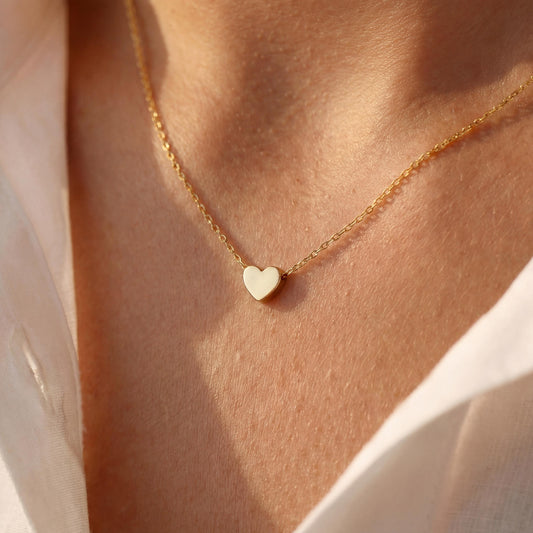 Minimalist 14k gold plated tiny puff heart necklace on a model wearing a white shirt, dainty gold choker chain detail, small heart pendant close up, perfect mothers day gift or birthday jewelry for her.