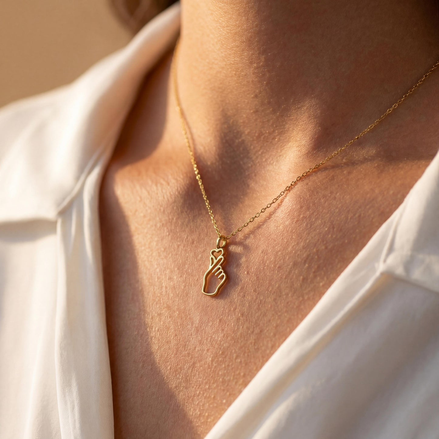 A woman wearing a dainty 14K gold minimalist Korean finger heart necklace, a delicate saranghae hand gesture pendant resting on her collarbone.