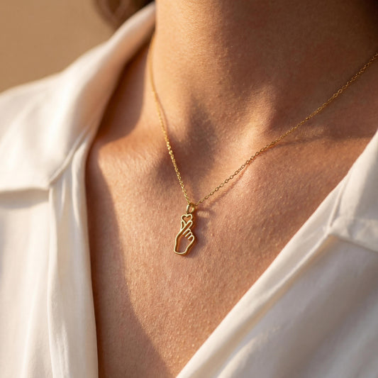 A woman wearing a dainty 14K gold minimalist Korean finger heart necklace, a delicate saranghae hand gesture pendant resting on her collarbone.