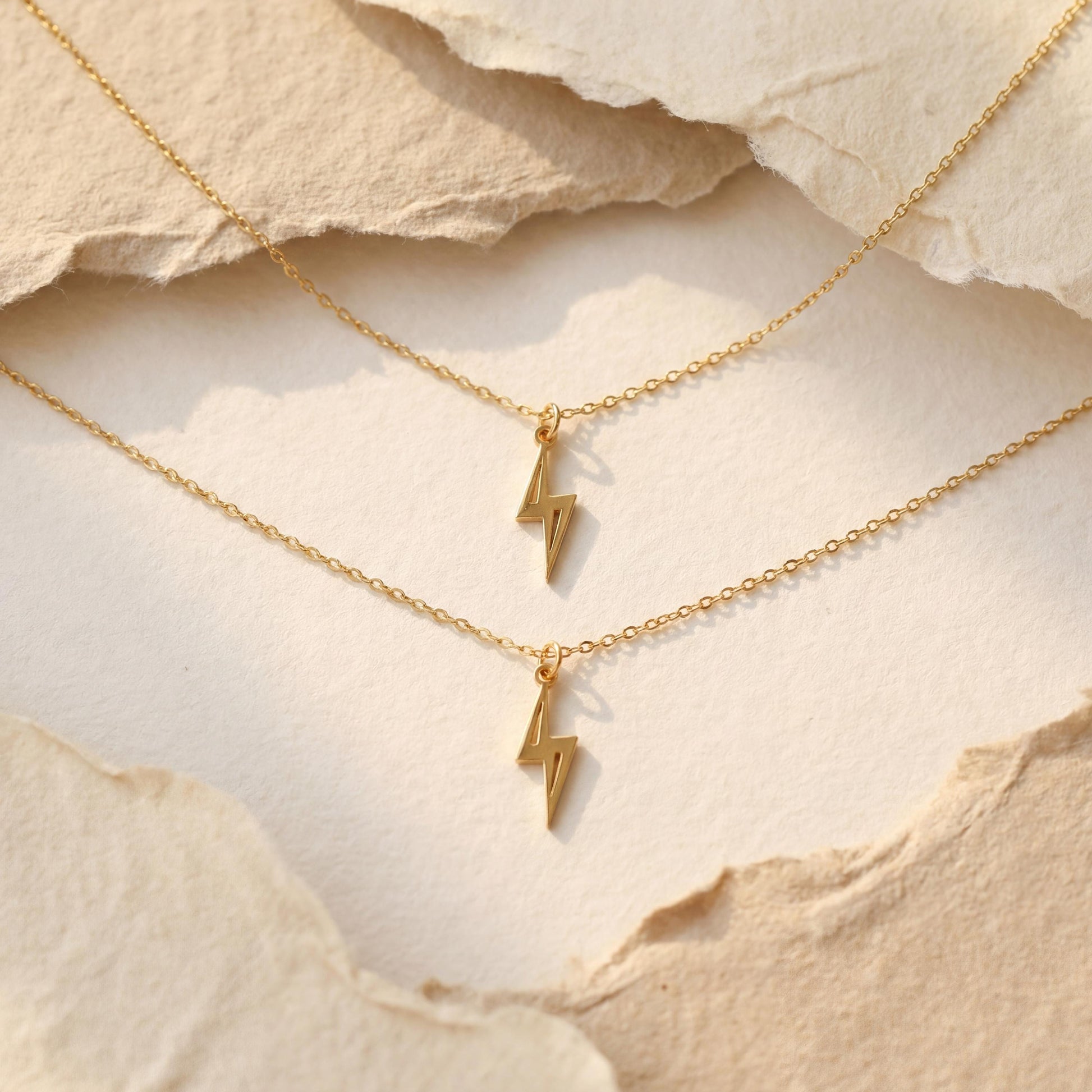 Close-up of a delicate minimalist 14k gold plated lightning bolt pendant necklace worn by a woman in a white shirt, glowing in soft sunlight.