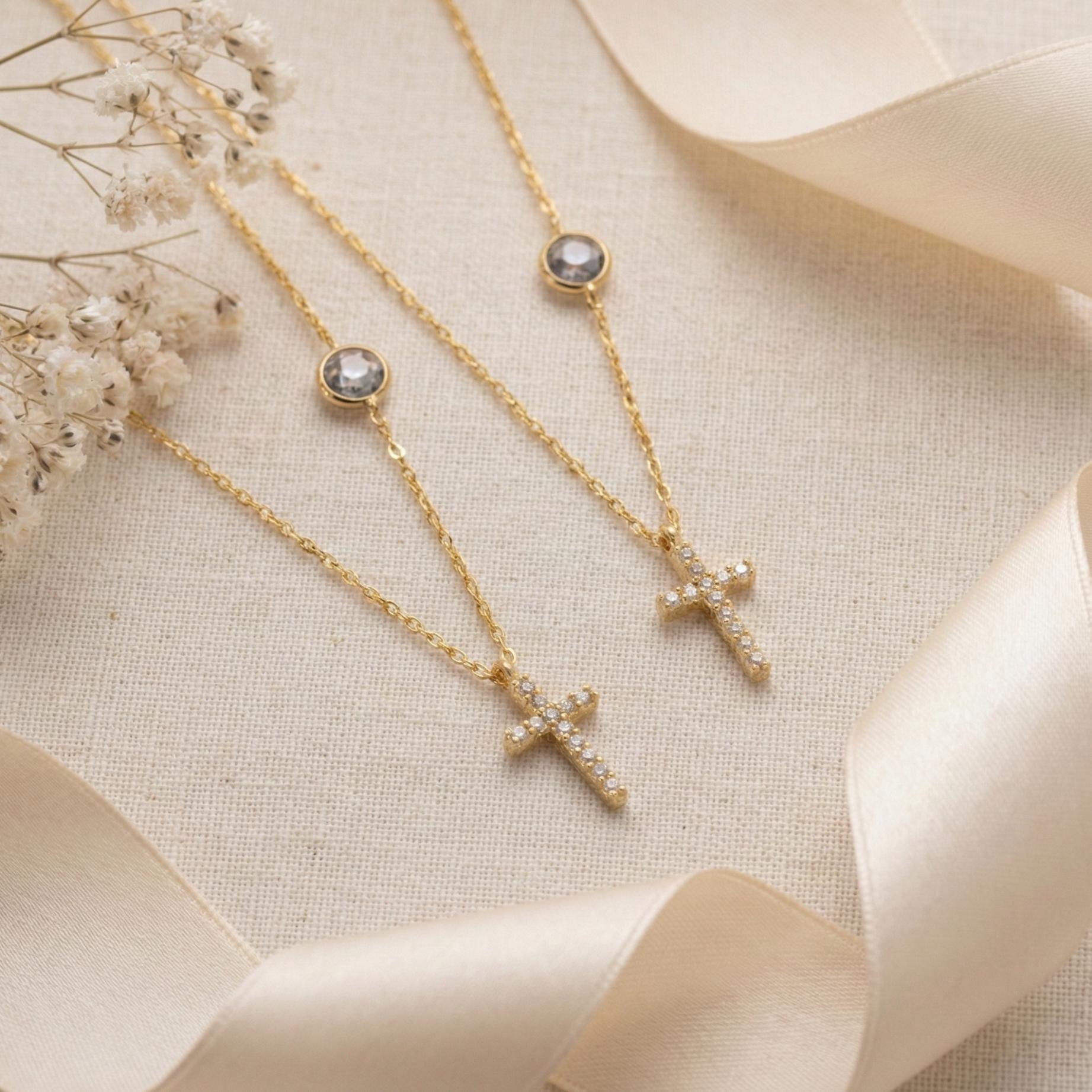 Dainty gold chain necklace featuring a small pave diamond cross pendant and a round bezel-set birthstone charm, worn by a model. Personalized minimalist religious jewelry.