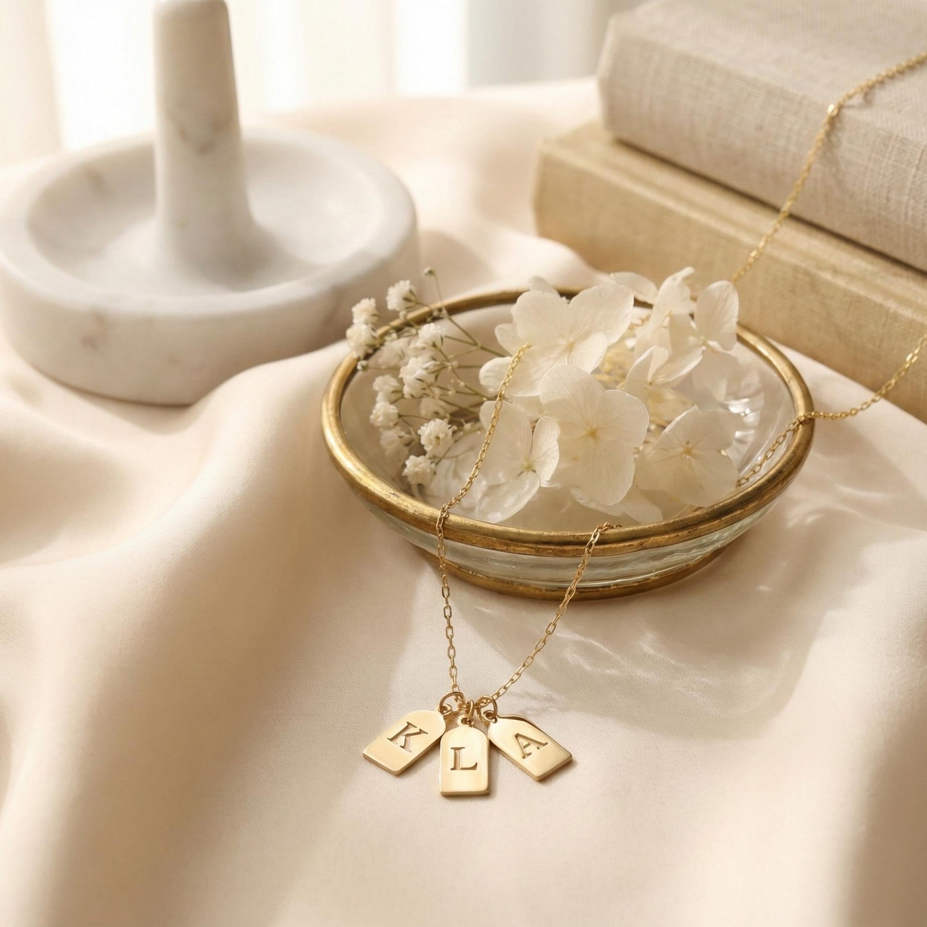 Gold initial necklace featuring three small rectangular pendant tags engraved with letters K L A, worn on a woman's neck, minimalist personalized jewelry for mom