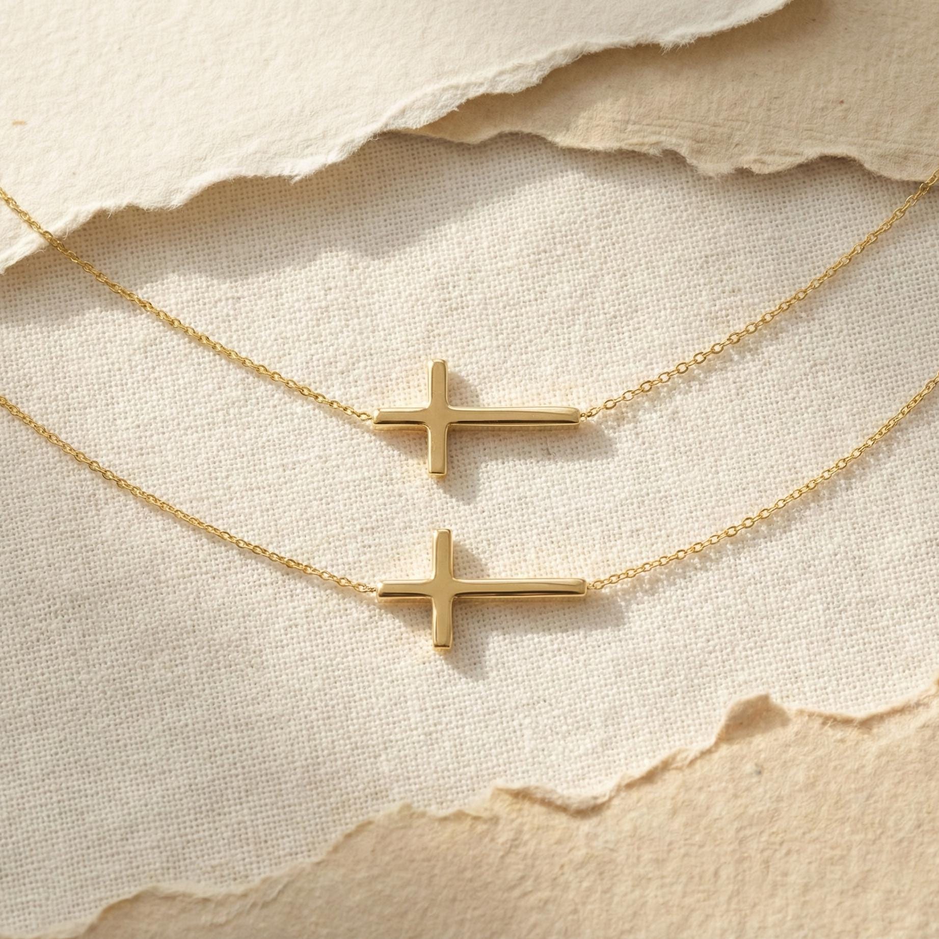 Close up of gold sideways cross pendant, delicate chain jewelry for layering, modern faith necklace flat lay