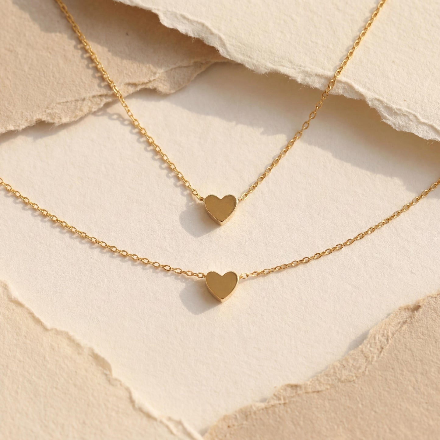 Minimalist 14k gold plated tiny puff heart necklace on a model wearing a white shirt, dainty gold choker chain detail, small heart pendant close up, perfect mothers day gift or birthday jewelry for her.