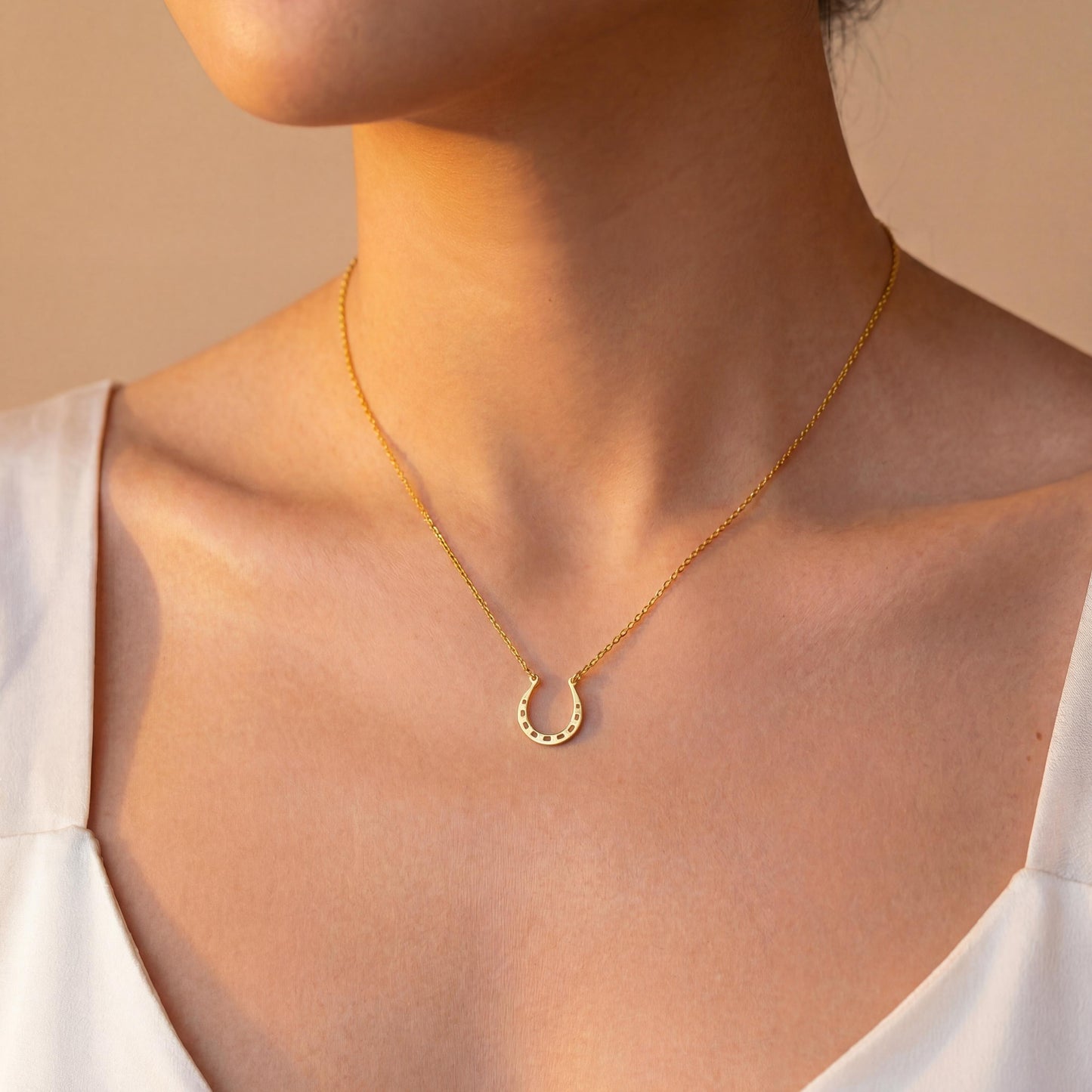 Dainty 14K gold horseshoe necklace worn delicately on a woman's neck, minimalist lucky charm pendant jewelry ideal for everyday wear and thoughtful Mother's day gift.