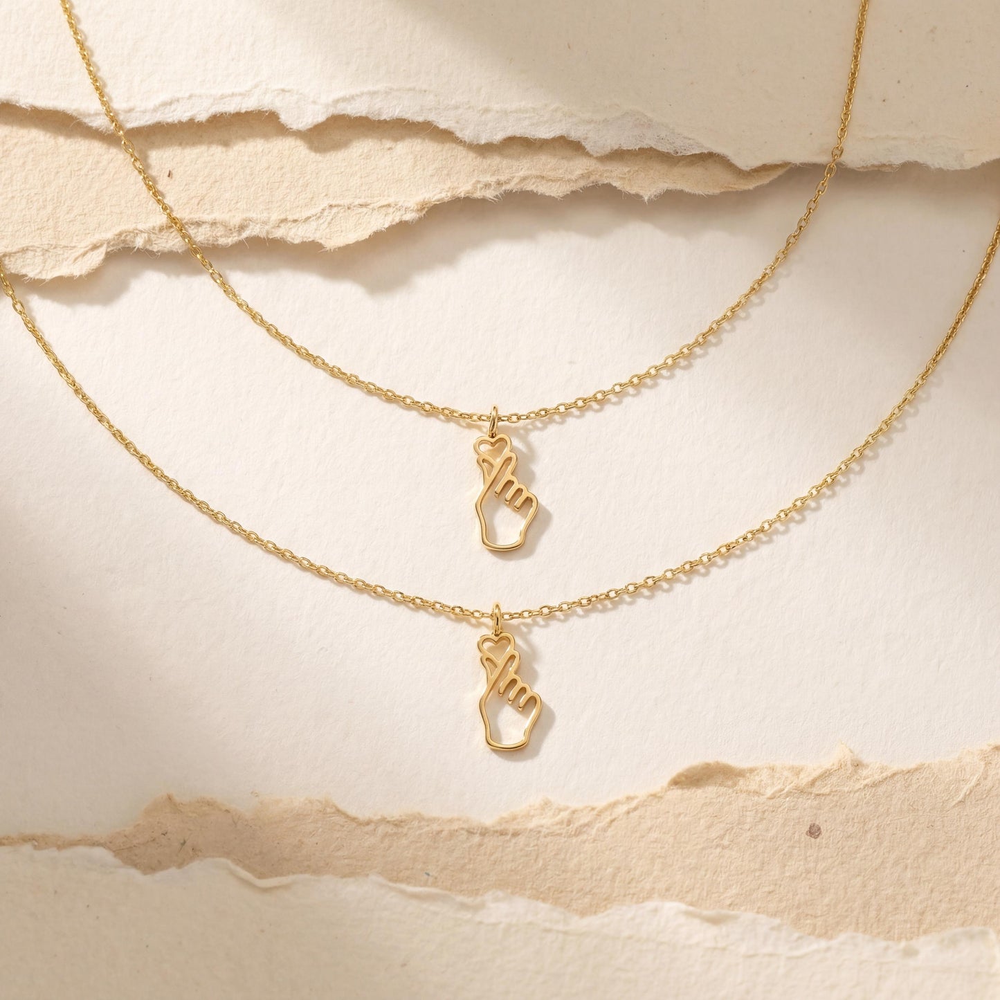 A woman wearing a dainty 14K gold minimalist Korean finger heart necklace, a delicate saranghae hand gesture pendant resting on her collarbone.