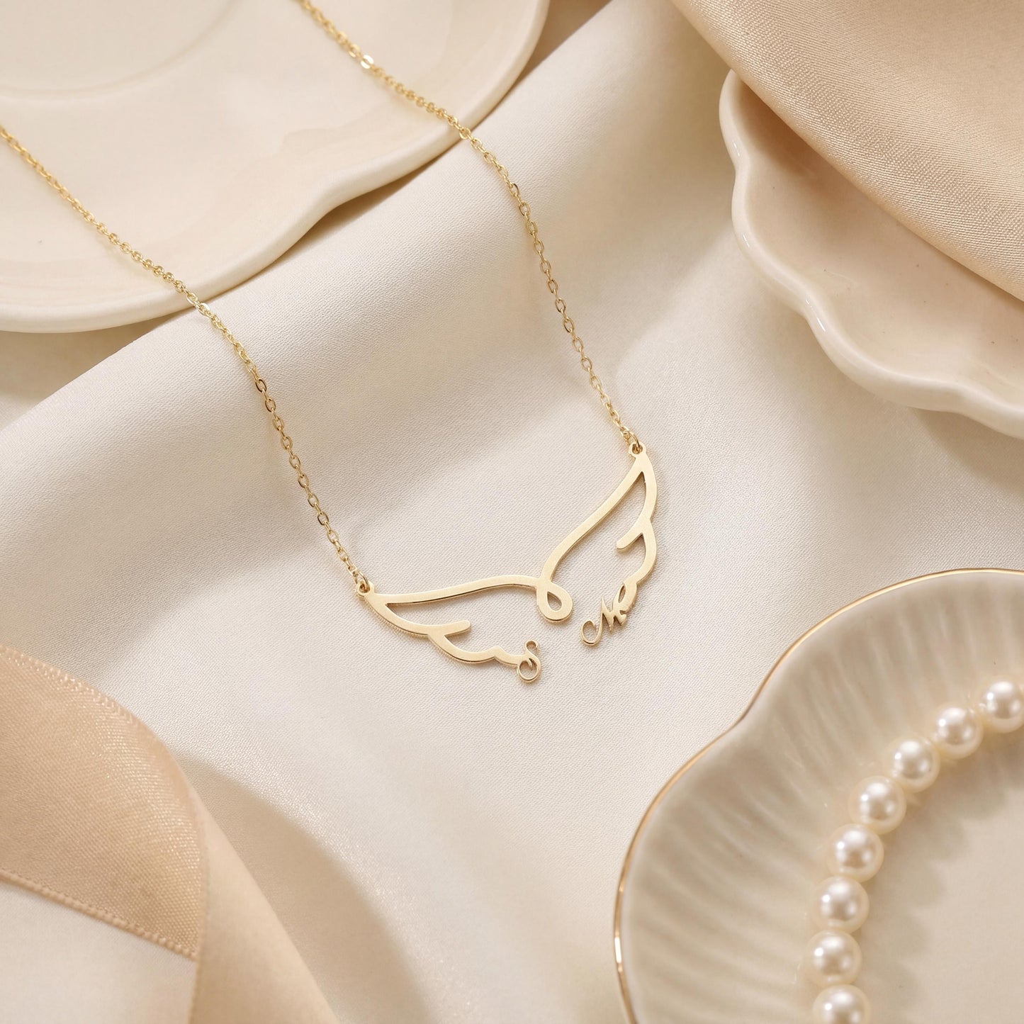 Dainty custom angel wing necklace featuring two personalized initial letters nesting at the bottom of the wings, worn on a woman's collarbone during golden hour.