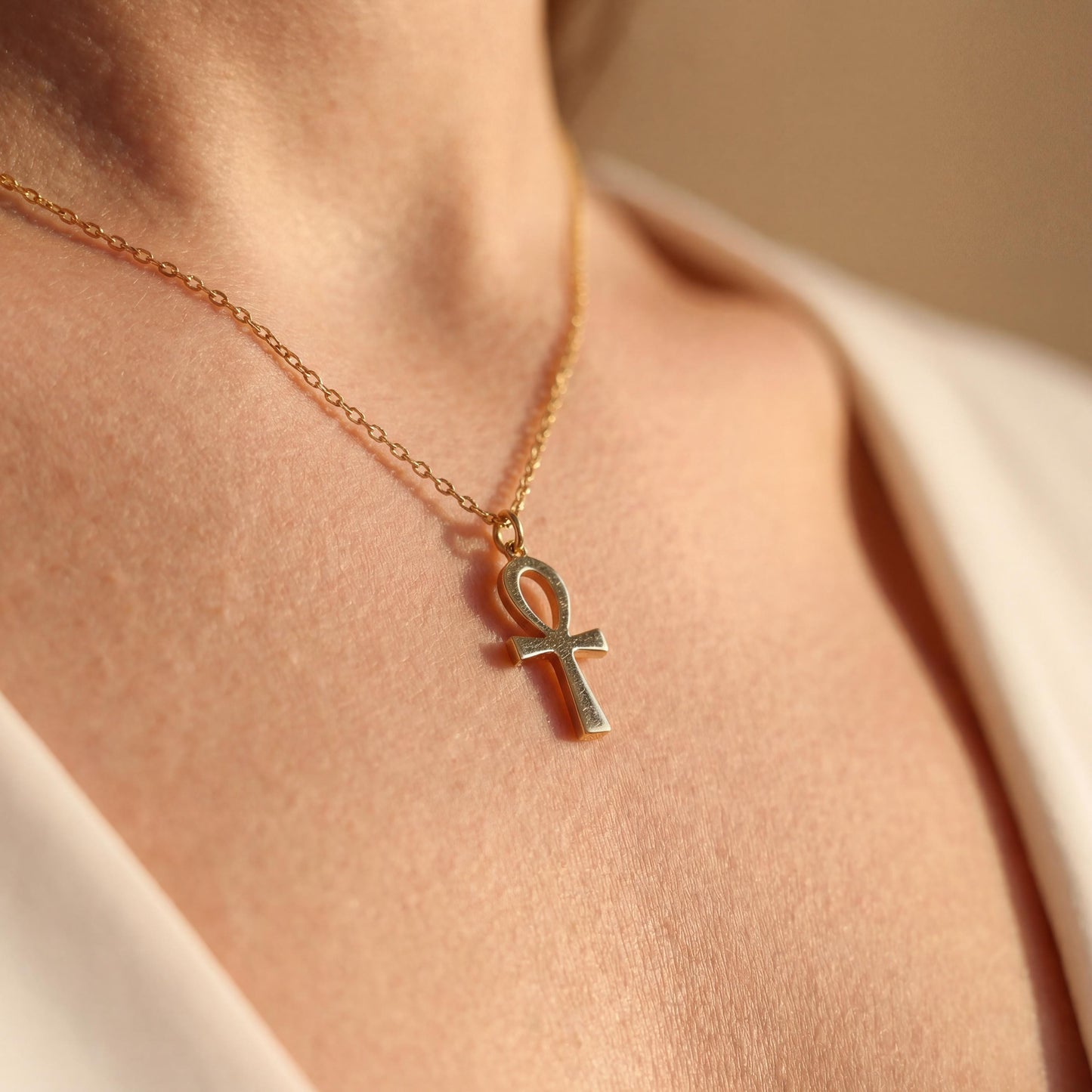 Minimalist Ankh necklace worn by a woman, dainty Egyptian cross key of life pendant resting on chest in natural sunlight, elegant everyday jewelry.