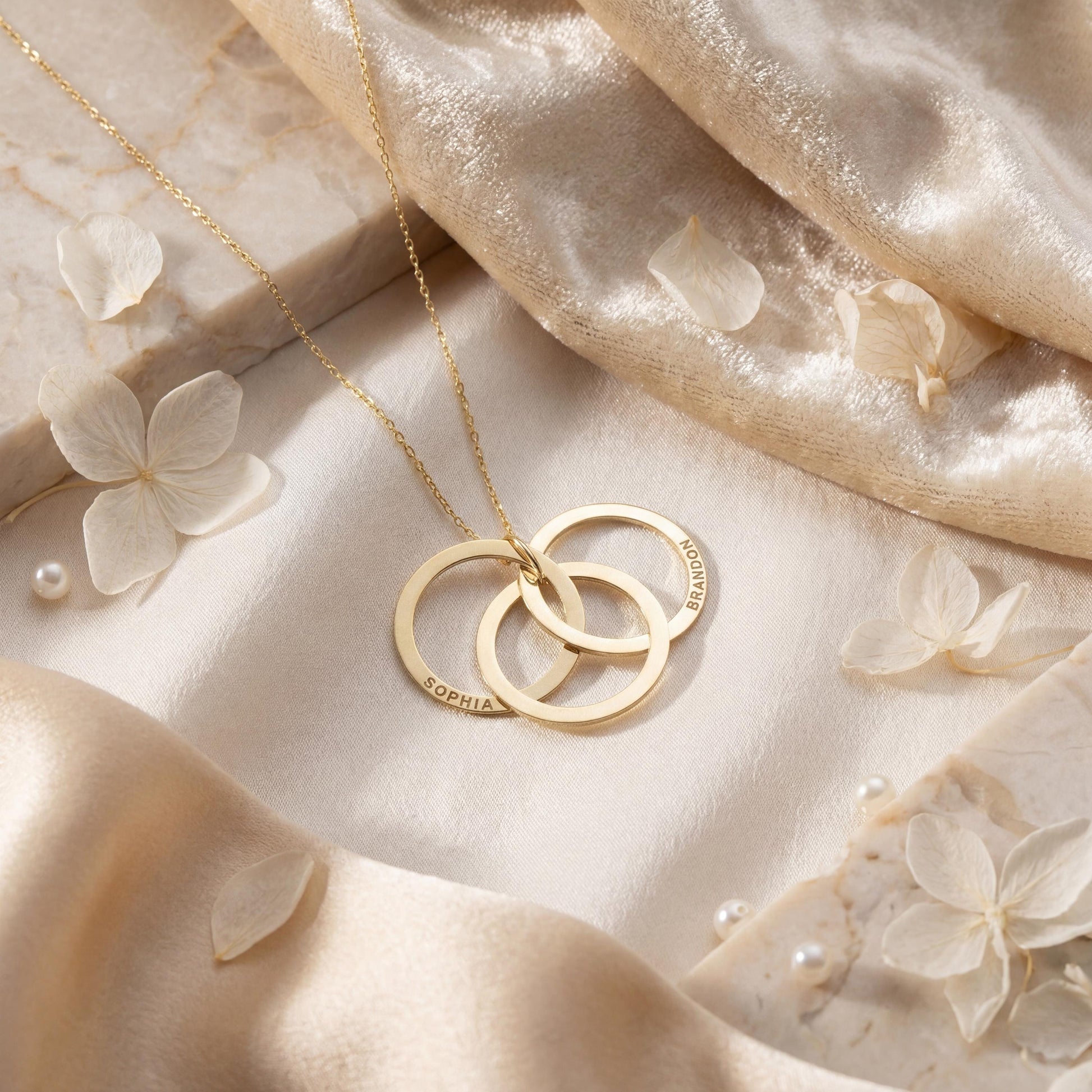 14K gold plated interlocking circle necklace featuring three beautifully intertwined rings, delicately custom engraved with the family names Sophia and Brandon, resting elegantly on a woman's collarbone.